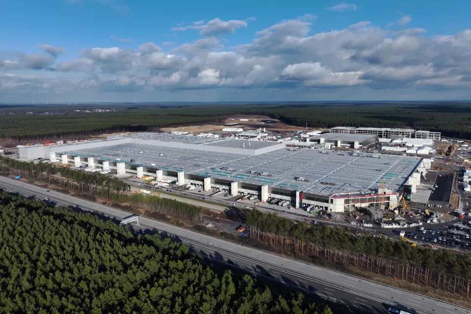 Birds-eye view of a large EV factory and nearby highway, all surrounded by forest.